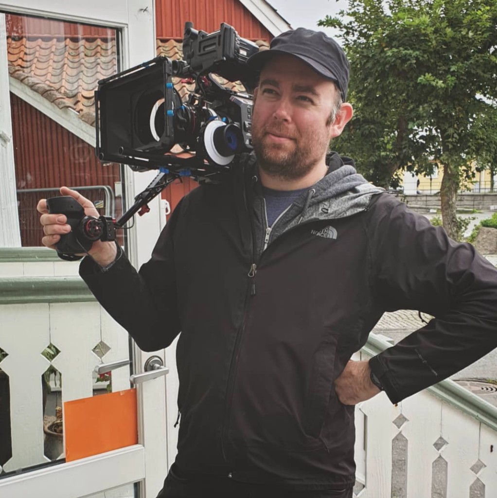 James Ian Gray with a cinema camera on his shoulder outdoors